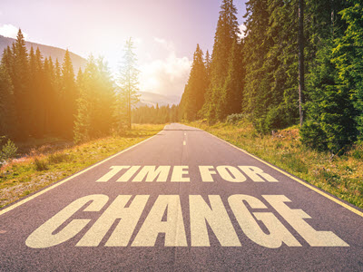 a road surrounded by trees on either side with the words "time to change" written in yellow on the road