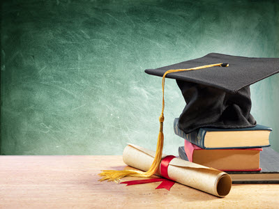 graduation cap sitting atop three books and beside a rolled up diploma tied with a red ribbon against a green chalkboard background