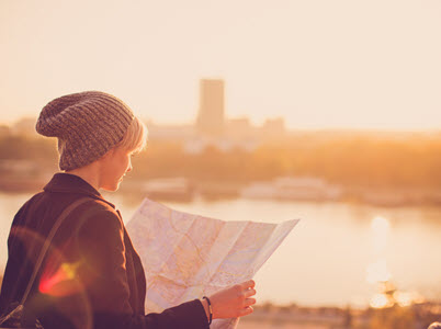 a person reading a map on the bank of a river with silohouttes of buildings on the opposing riverbank