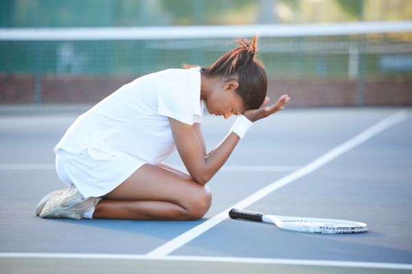 distraught female tennis player kneeling on court