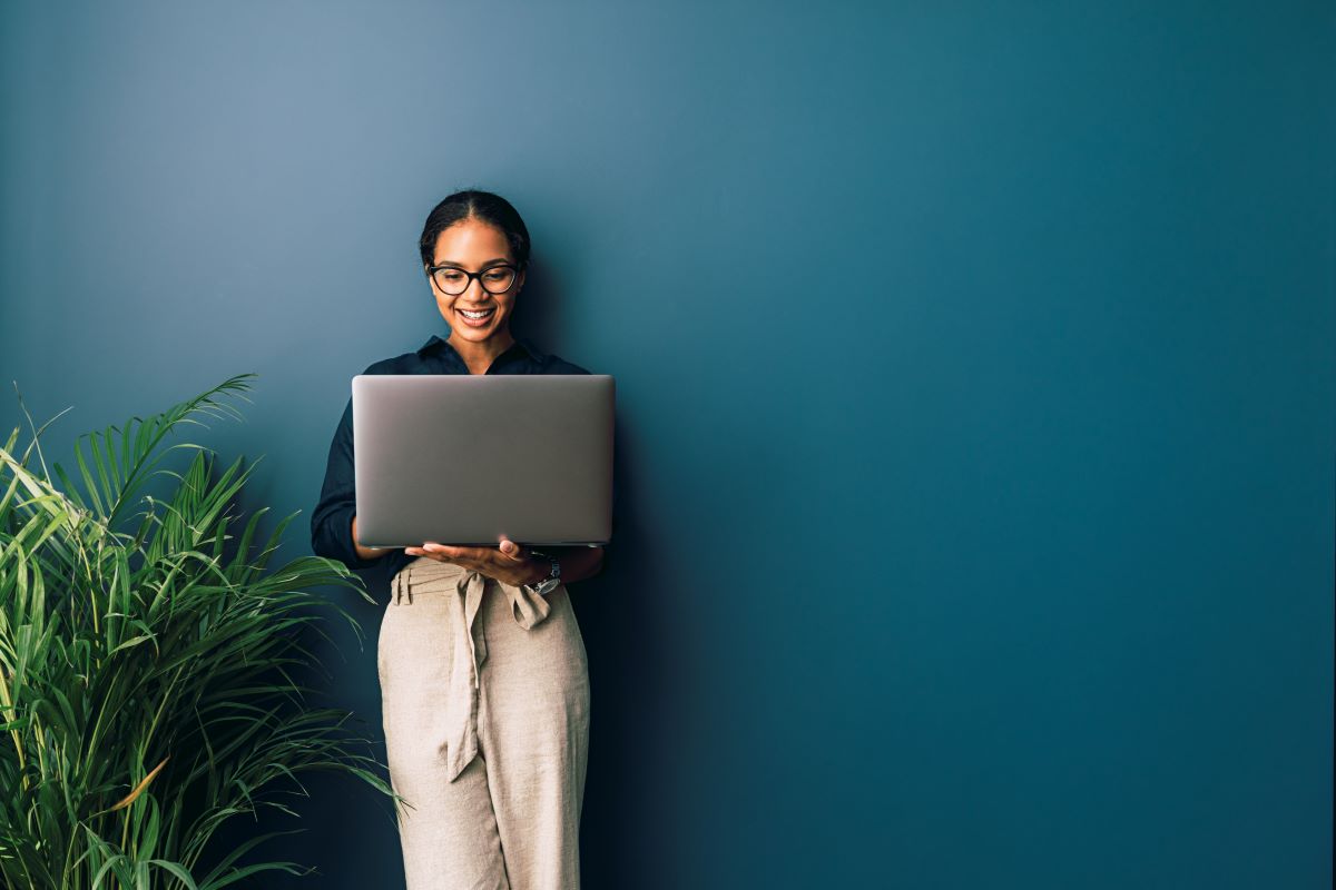 student standing against wall looking at laptop