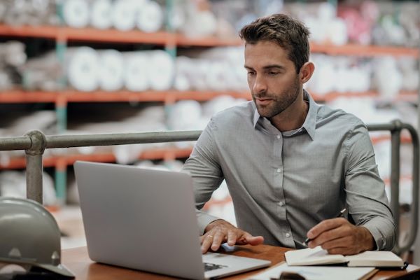 supply chain manager sitting in warehouse working on laptop