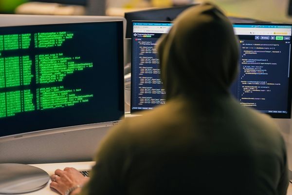 cybercriminal wearing hood looking at code on computer