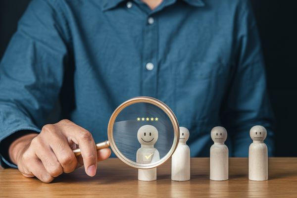 hand holding magnifying glass in front of wooden figure